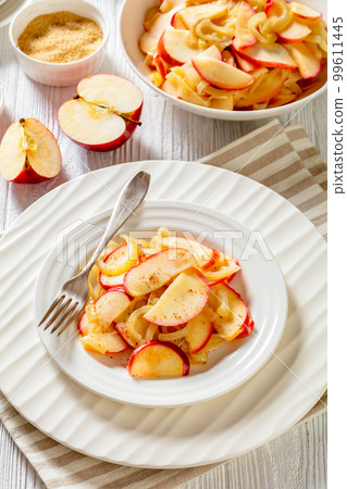 fried onion and red apple slices on white plate with fork on white wood table 99611445