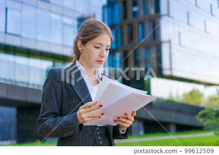 Young business woman holding papers in business clothes on city street against 99612509