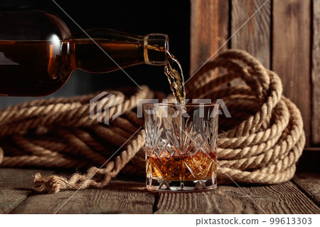 Rum, cognac, or whiskey is poured into a crystal glass. Rum, cognac, or whiskey is poured into a crystal glass. 99613303