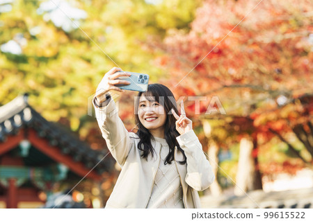 一位女士用智能手機拍照，背景是秋葉 99615522