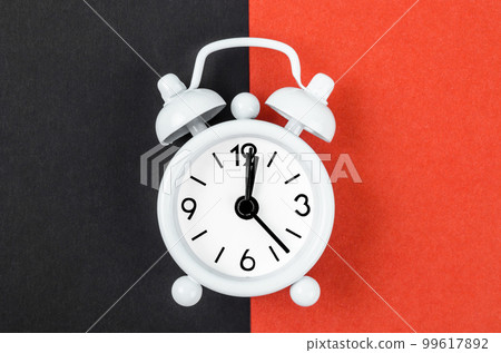 A White vintage alarm clock on bright red and black colour background. A White vintage alarm clock on bright red and black colour background. 99617892