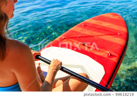 Woman sitting on sup board and enjoying peace and quiet outdoors 99618219