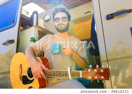 Young man sits on the doorstep of trailer truck and playing guitar Young man sits on the doorstep of trailer truck and playing guitar 99618231