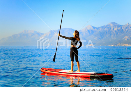 Woman paddling on sup board with mountains on background Woman paddling on sup board with mountains on background 99618234