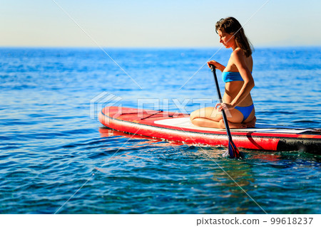 Woman sitting on sup board and enjoying peace and quiet outdoors Woman sitting on sup board and enjoying peace and quiet outdoors 99618237