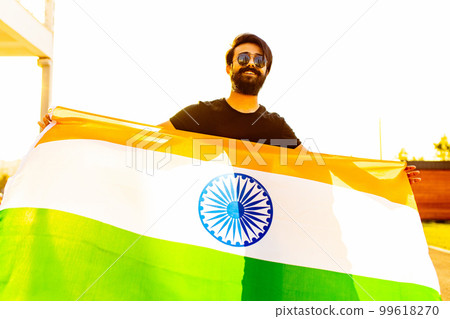 handsome indian bearded man in black cotton t-shirt wawing indian flag in summer park at sunset golg light handsome indian bearded man in black cotton t-shirt wawing indian flag in summer park at sunset golg light 99618270