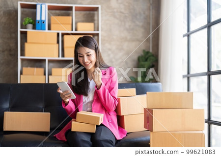 Startup SME small business entrepreneur of freelance Asian woman using a laptop with box Cheerful success happy Asian woman her hand lifts up online marketing packaging and delivery SME idea concept 99621083