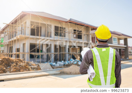 young professional engineer in protective helmet and blueprints paper at the house building construction site young professional engineer in protective helmet and blueprints paper at the house building construction site 99623873