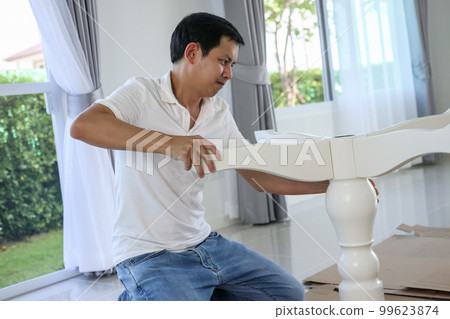 Asian man assembling white table furniture at home Asian man assembling white table furniture at home 99623874