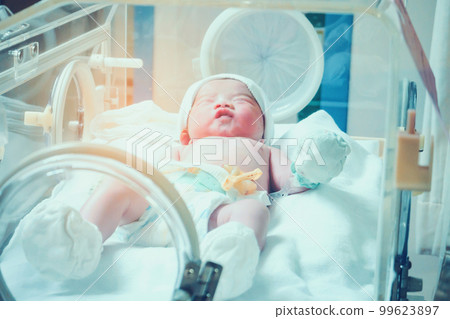 Newborn baby girl inside incubator in hospital post delivery room 99623897