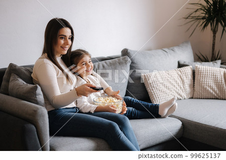 Little girl watching a cartoon with her mother. Daughter eating popcorn and smile. Home mood 99625137