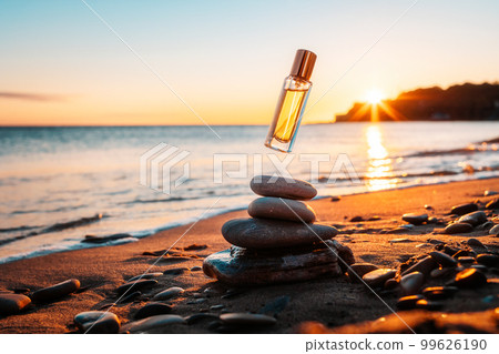 A golden transparent glass perfume bottle with a gold lid hovers over a pyramid of stones. Sandy beach and sunset in the background. Copy space. Perfume advertising concept 99626190