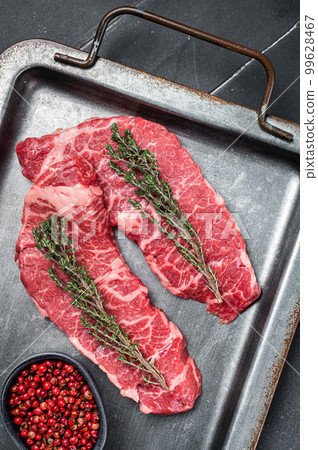 Uncooked Raw Denver beef meat Steak with pink pepper and thyme on a steel tray. Black background. Top view Uncooked Raw Denver beef meat Steak with pink pepper and thyme on a steel tray. Black background. Top view 99628467