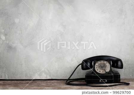Retro black rotary telephone on wooden table in front gray concrete background 99629700