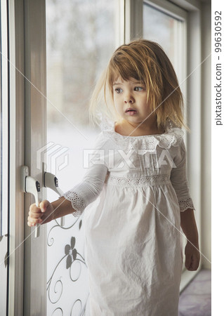 Adorable baby in a nightgown on the windowsill Adorable baby in a nightgown on the windowsill 99630592