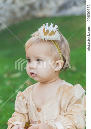 charming baby in princess costume walks near the castle at sunset 99630681