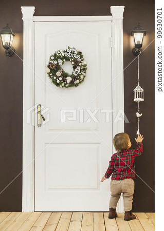 adorable baby stands at the front door with a christmas wreath adorable baby stands at the front door with a christmas wreath 99630701