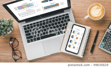 Laptop computer and smart phone with charts and reports on screen display on office desk workplace. Top view flat lay Laptop computer and smart phone with charts and reports on screen display on office desk workplace. Top view flat lay 99630829