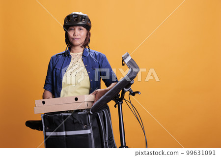 Old pizzeria delivery employee delivering takeout pizza in cardboard box to client, using bike as work transportation. Restaurant worker wearing blue t shirt and cap while working as courier Old pizzeria delivery employee delivering takeout pizza in cardboard box to client, using bike as work transportation. Restaurant worker wearing blue t shirt and cap while working as courier 99631091