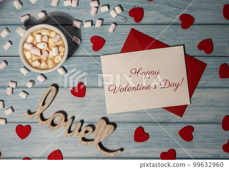 HAPPY VALENTINES DAY text Greeting card with red envelope with white cup of coffee and marshmallows on wooden background. Romantic Small hearts Valentine day. Holiday morning HAPPY VALENTINES DAY text Greeting card with red envelope with white cup of coffee and marshmallows on wooden background. Romantic Small hearts Valentine day. Holiday morning 99632960