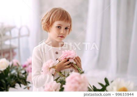 Girl 6-7 years old in a white dress holds a flower Girl 6-7 years old in a white dress holds a flower 99633944