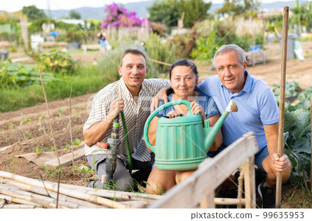 Happy elderly couple with adult son posing in homestead garden 99635953