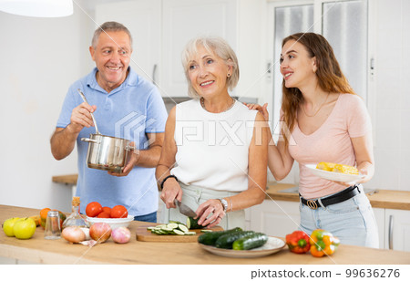 Portrait of mature man, woman and daughter preparing family dinner at kitchen table 99636276