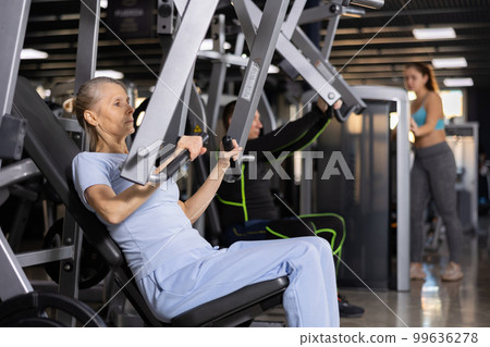 Focused mature female athlete using chest press machine in gym 99636278