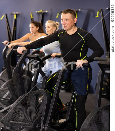 Group of people engaged in a spin bike simulator in the gym, exercising on stationary bike 99636386