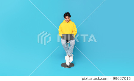 Korean Teen Guy Using Laptop Sitting Over Blue Studio Background Korean Teen Guy Using Laptop Sitting Over Blue Studio Background 99637015