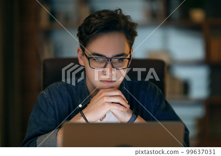 Focused IT worker looking at laptop screen, working late at office Focused IT worker looking at laptop screen, working late at office 99637031