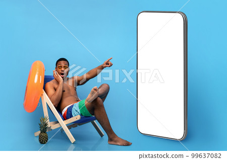 Black guy in swimwear sitting in chair, pointing at phone Black guy in swimwear sitting in chair, pointing at phone 99637082