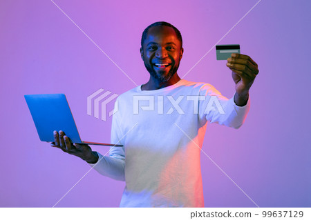 Positive handsome black man using computer, showing credit card Positive handsome black man using computer, showing credit card 99637129