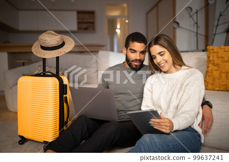 Smiling young arab male, european lady use tablet and laptop to choose country for vacation travel, buy tickets Smiling young arab male, european lady use tablet and laptop to choose country for vacation travel, buy tickets 99637241