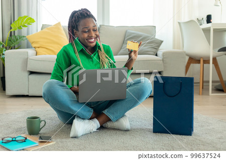 Online shopping concept. Happy black woman showing credit card and using laptop, ordering clothes via internet Online shopping concept. Happy black woman showing credit card and using laptop, ordering clothes via internet 99637524