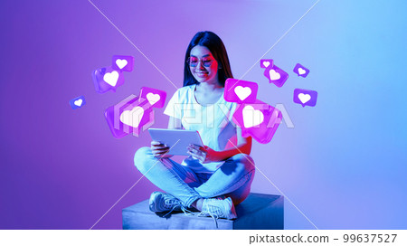 Smiling young asian woman in glasses typing on tablet, has romantic chat with hearts on neon background Smiling young asian woman in glasses typing on tablet, has romantic chat with hearts on neon background 99637527