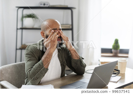 Tired black male rubbing eyes, suffering from overwork, discomfort long hours of sedentary in home office interior 99637541