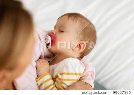 Small baby girl on mother's hands sucking pacifier and sleeping peacefully, above view, closeup Small baby girl on mother's hands sucking pacifier and sleeping peacefully, above view, closeup 99637550