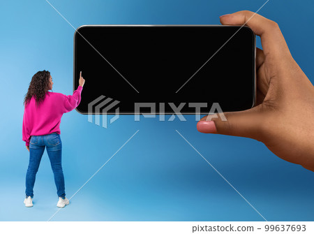 Back view of black woman touching blank smartphone screen in huge hand 99637693