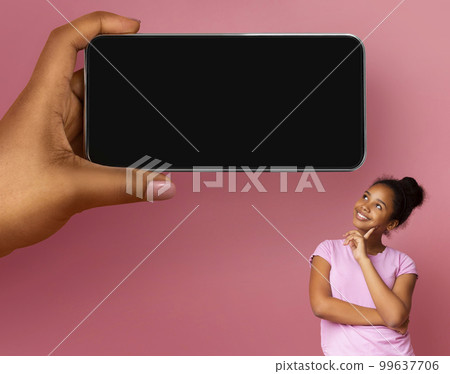 Dreamy Teen Black Girl Looking At Blank Cellphone In Huge Female Hand 99637706