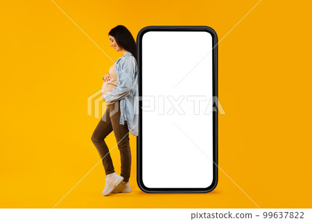 Happy pregnant woman leaning on huge blank cellphone and hugging her belly, advertising mobile app or website, mockup Happy pregnant woman leaning on huge blank cellphone and hugging her belly, advertising mobile app or website, mockup 99637822