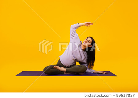 Active pregnancy concept. Happy future mom doing her morning yoga workout on mat over yellow studio background Active pregnancy concept. Happy future mom doing her morning yoga workout on mat over yellow studio background 99637857