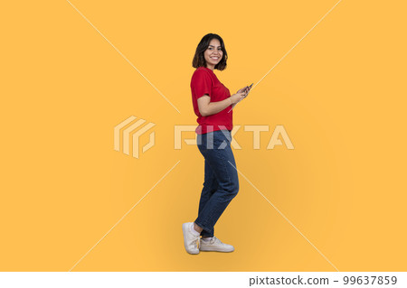 Positive arab woman using smartphone on yellow Positive arab woman using smartphone on yellow 99637859