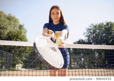 Tennis player woman holding a racket. Caucasian woman playing tennis on the court outdoors. Woman wearing blue sport dress and posing for a photo. 99640456