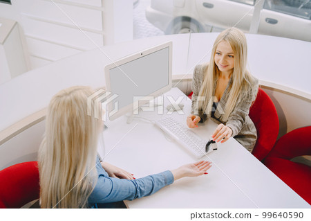 Ladies in a car salon. Woman buying the car. Elegant woman in a blue dress. Manager helps the client. 99640590