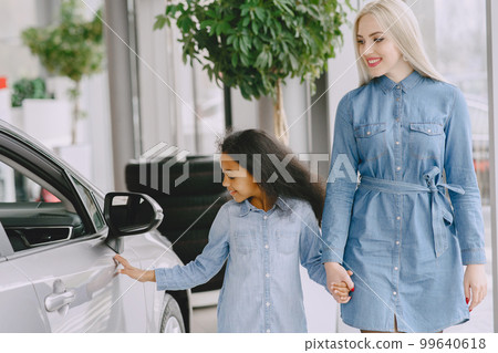 Family in a car salon. Woman buying the car. Little african girl with mther. 99640618
