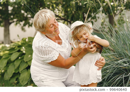 Family in a back yeard. Granddaughter with grandmother. People with little chicken. 99640640