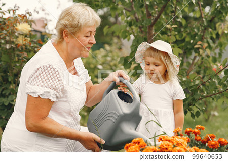 Small girl with senior grandmother gardening in the backyard garden. Child in a white hat. 99640653
