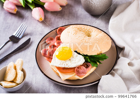 Fried egg heart, tomatoes, cheese and parsley in a bagel on a plate. Romantic breakfast. 99641766