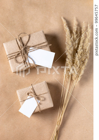 empty white gift tag mock up on craft paper box with dried spikelets decoration on natural beige background. 99645757